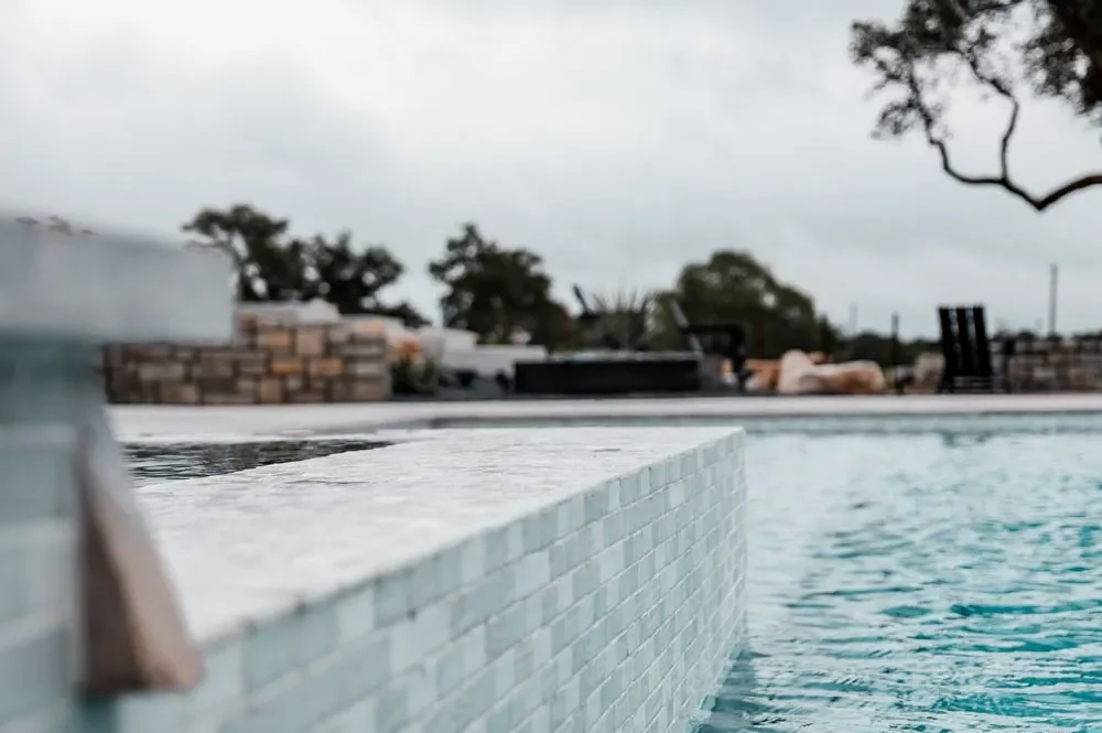 Close-up of a serene swimming pool edge and surface, with cloudy skies and trees in the background, creating a calming atmosphere